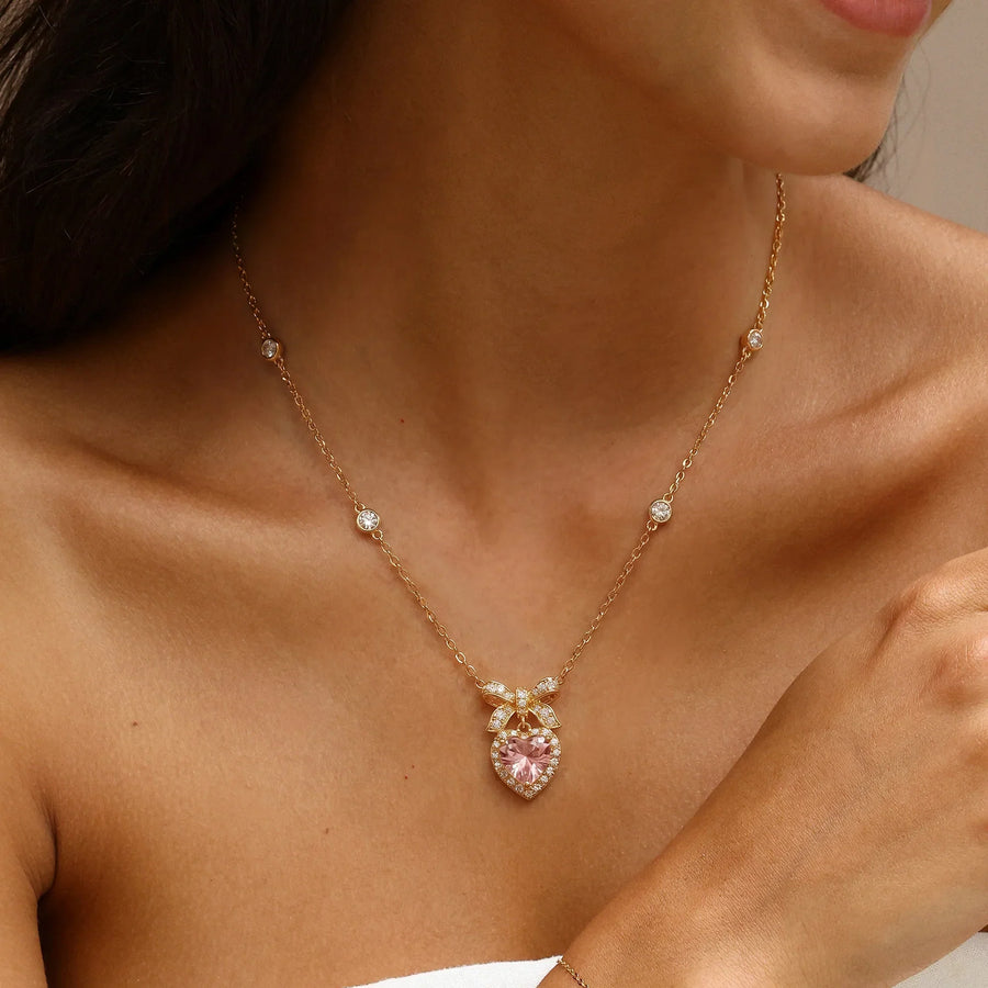 Gold dainty necklace with bow and pink heart cubic zirconia pendant worn on woman