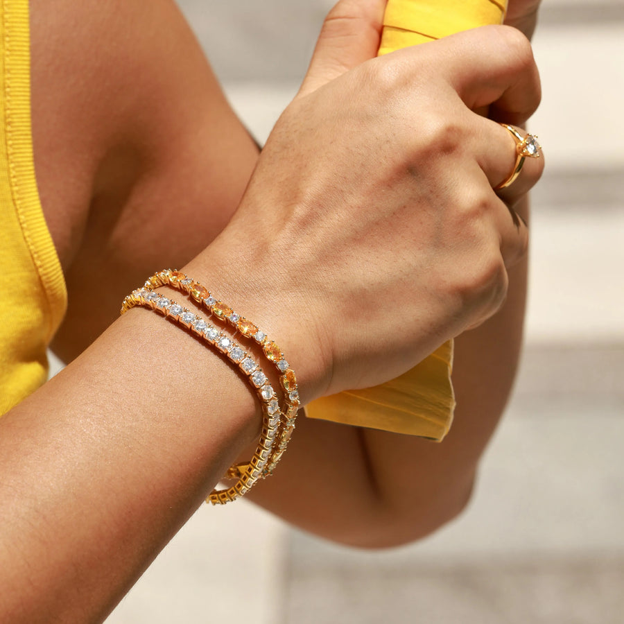 Woman wearing two layered gold tennis bracelets with clear and orange gemstones on wrist